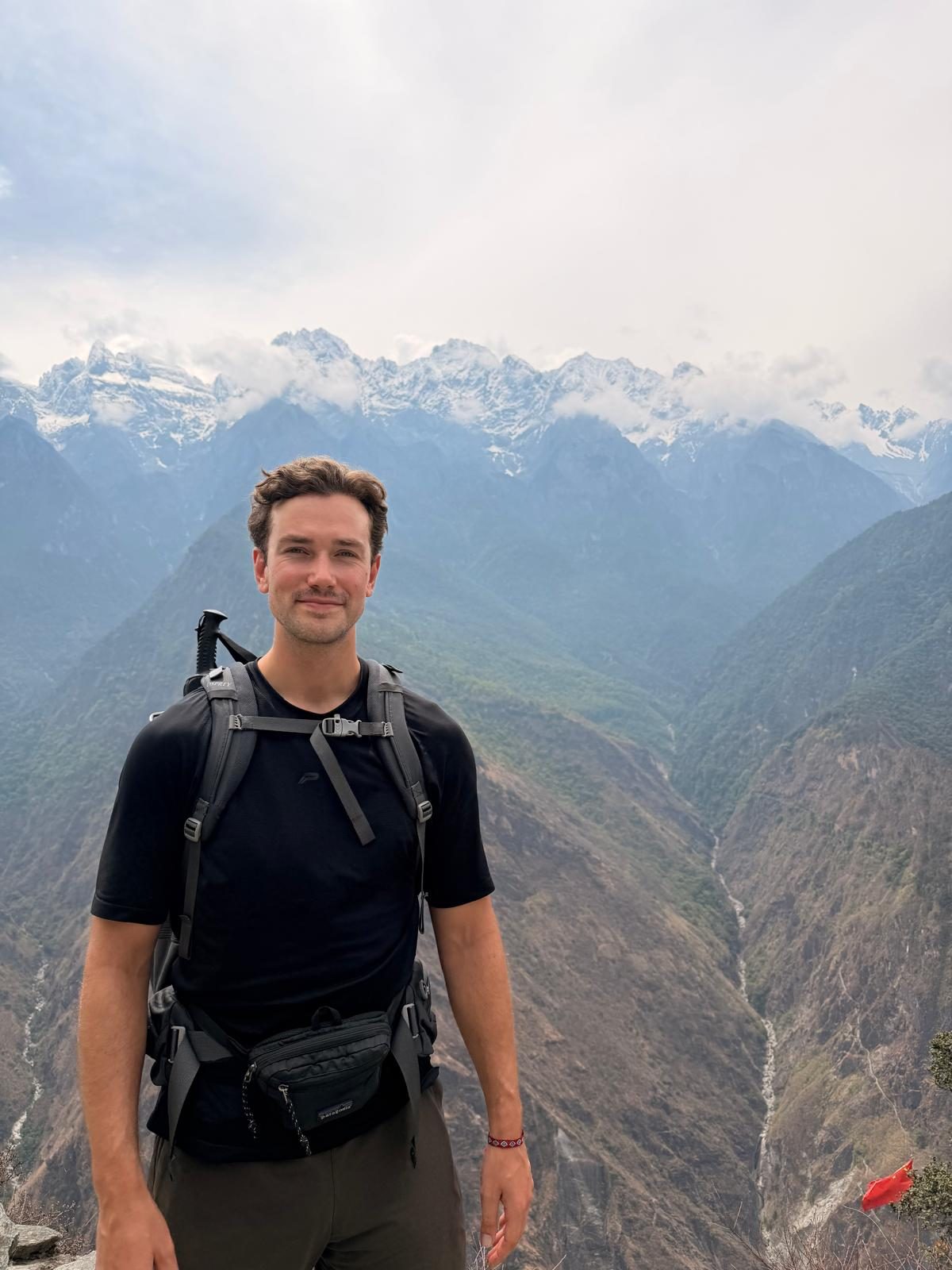 Sebastiaan standing on a mountain trail with snow-capped peaks behind him