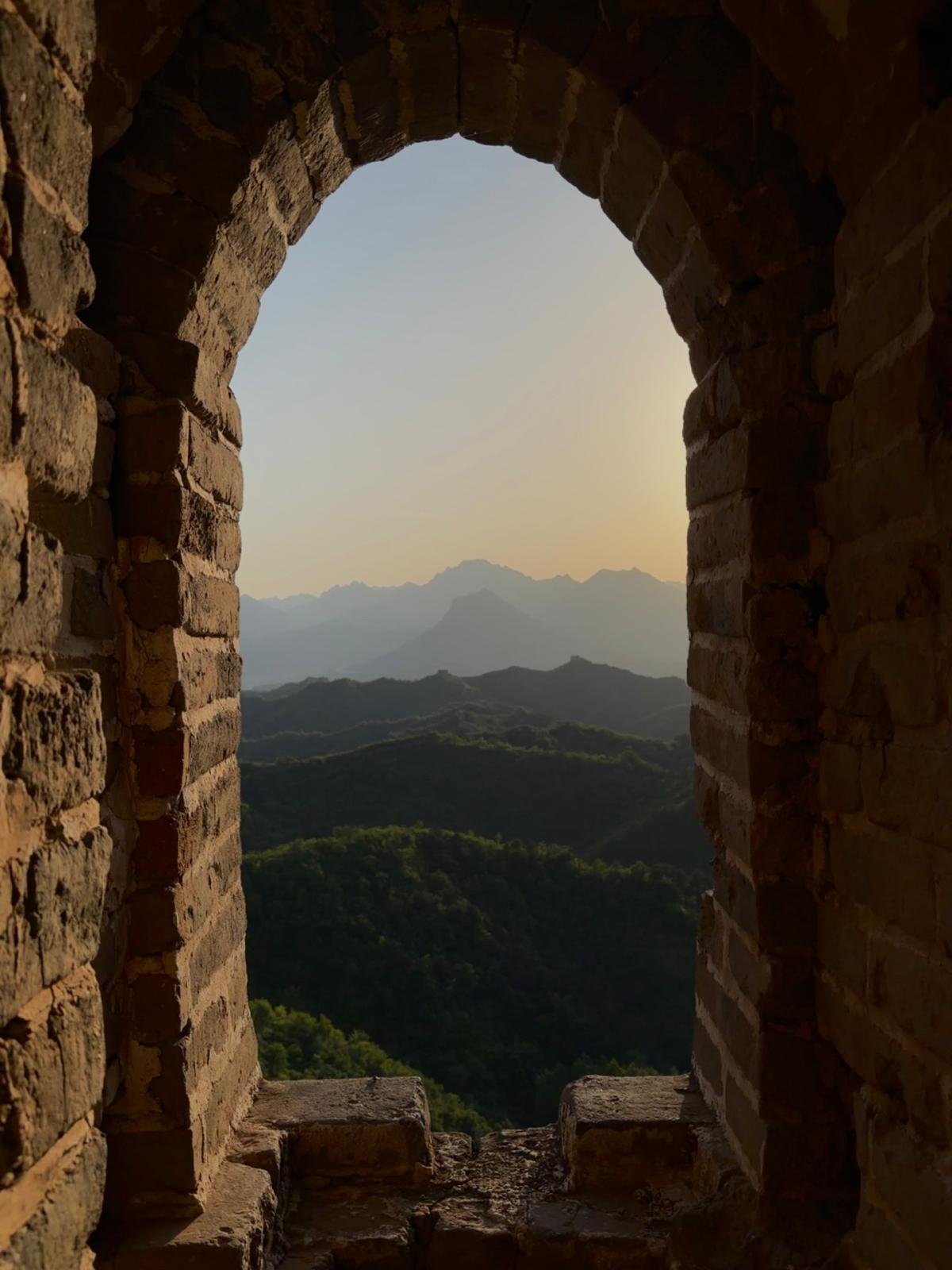 A stone archway on the Great Wall of China framing a mountain view at sunset